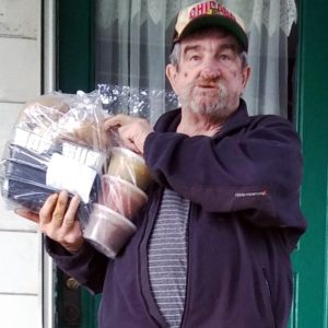 Client Robert, a veteran, standing at his door holding a bag of meals